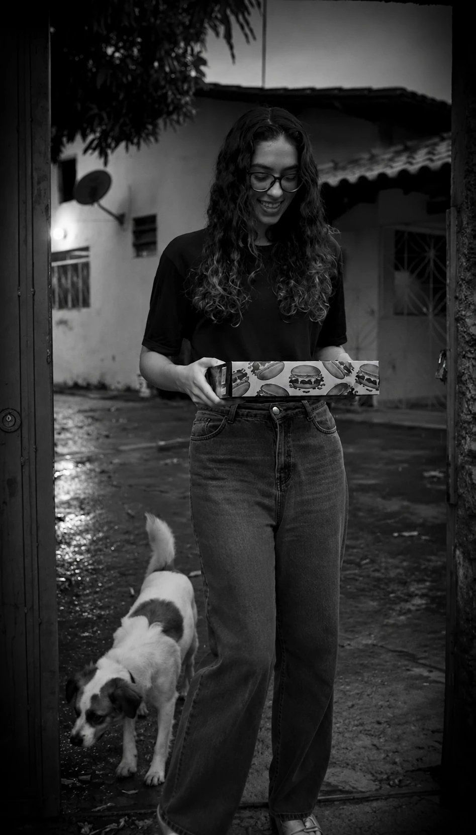 Dienne Braga, dona do HC Burger, sorrindo com uma caixa de hambúrguer no portão de casa